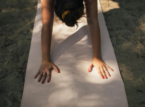 dettaglio di figura di donna che esegue una posizione di yoga su un tappetino, illuminata dalla luce del sole.